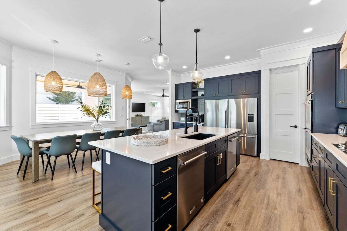 A modern kitchen with a central island, dark cabinetry, stainless steel appliances, and pendant lighting.