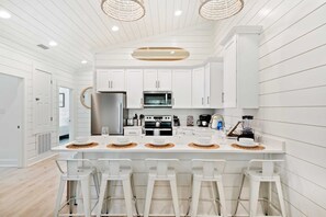 Une cuisine moderne avec des meubles blancs, un îlot central doté de tabourets et un réfrigérateur en acier inoxydable.
