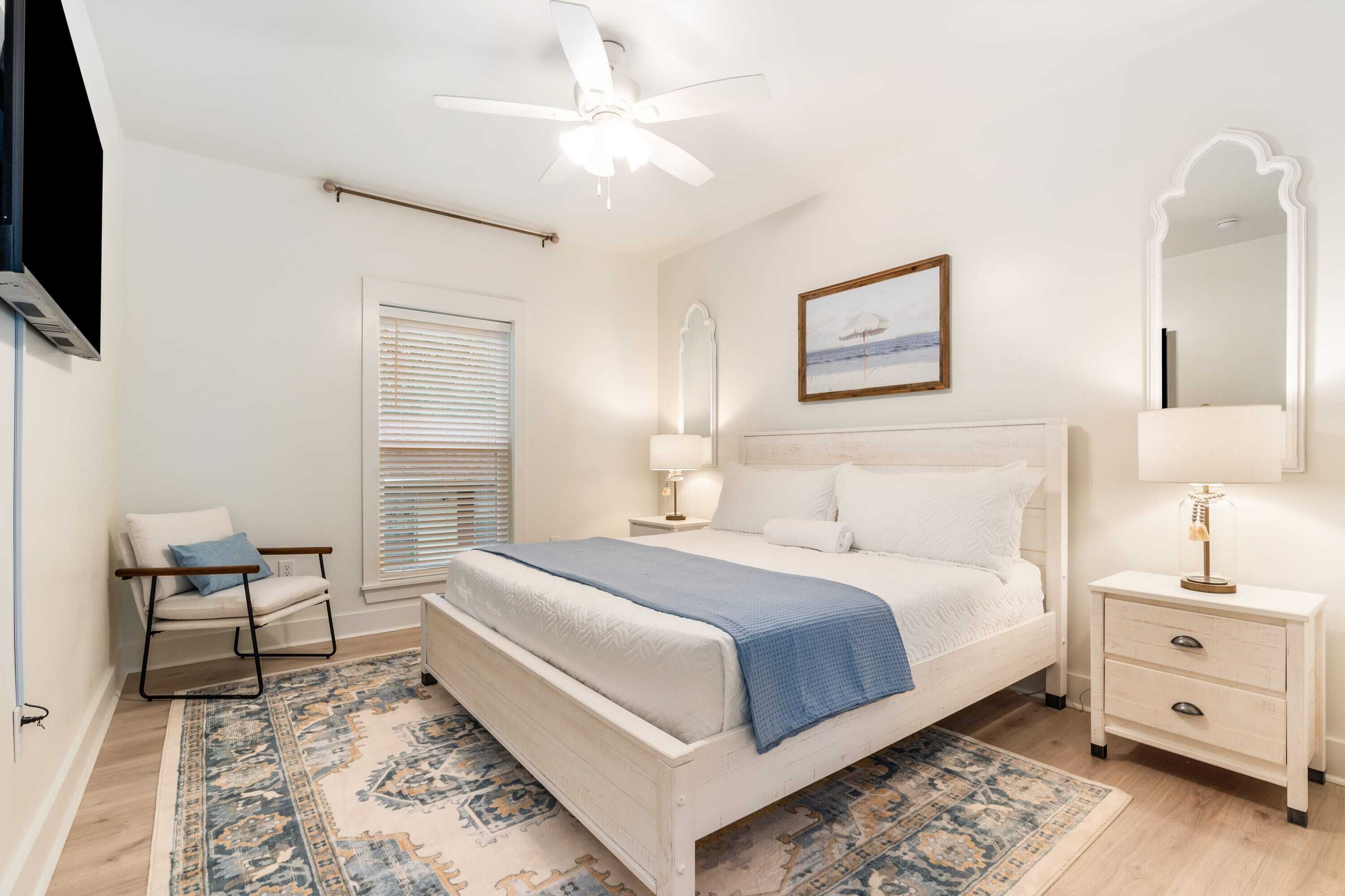 A bedroom with a bed, nightstands, a chair, a ceiling fan, and a window with blinds.