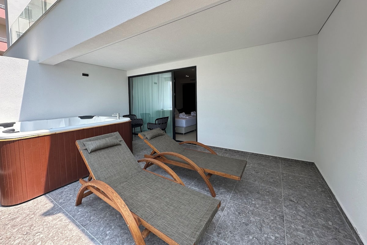 Ein modernes Hotelzimmer mit Balkon, einem Holztisch, zwei Sessel und einem Bett.