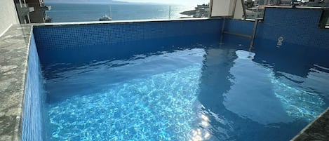 A clear blue pool with a view of the sea and mountains in the background.