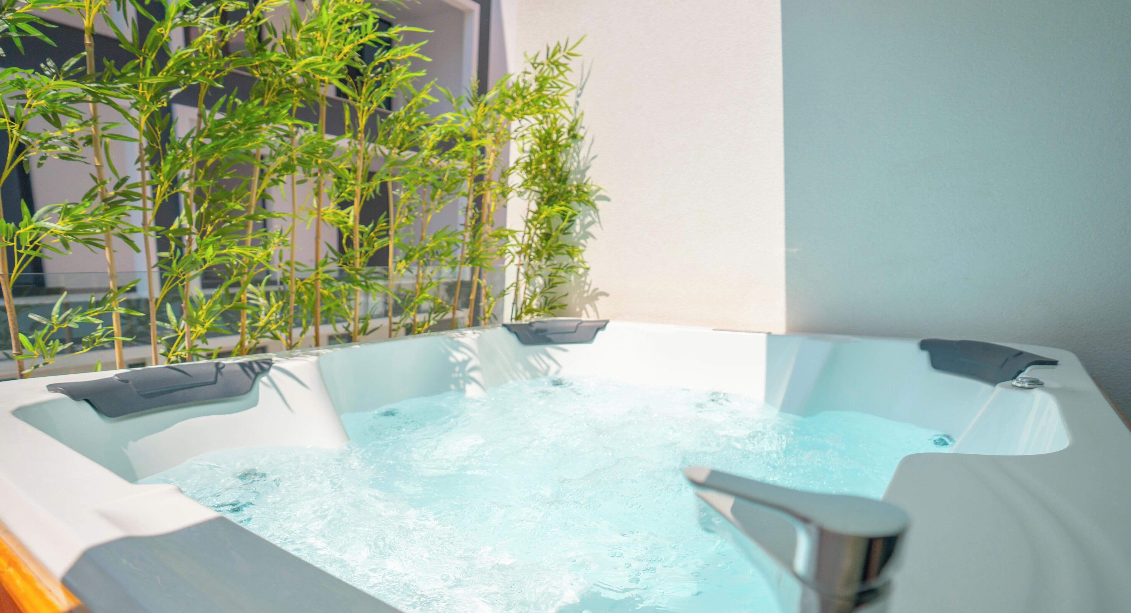 Ein Whirlpool mit Wasser, umgeben von Bambuspflanzen, und ein modernes Gebäude im Hintergrund.