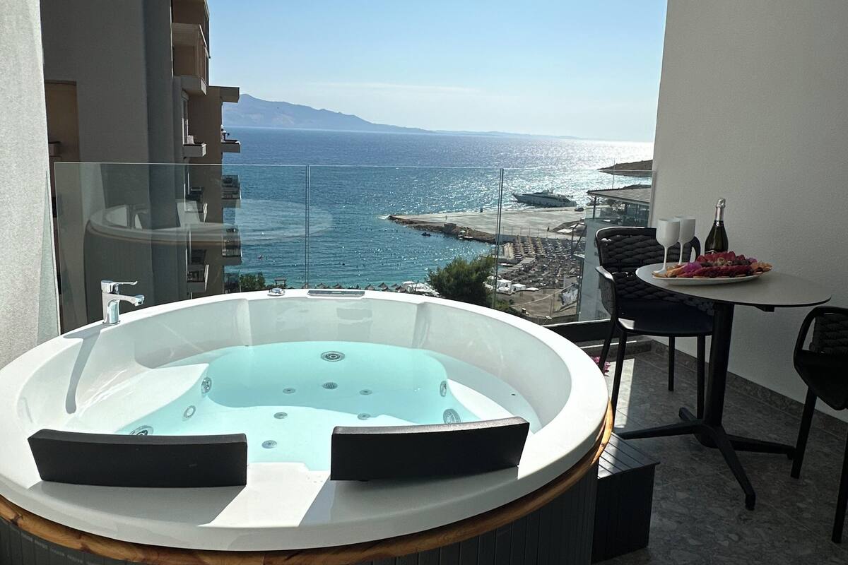 Ein Balkon mit Whirlpool, einem Esstisch mit Stühlen und Blick auf das Meer und die entfernten Berge.