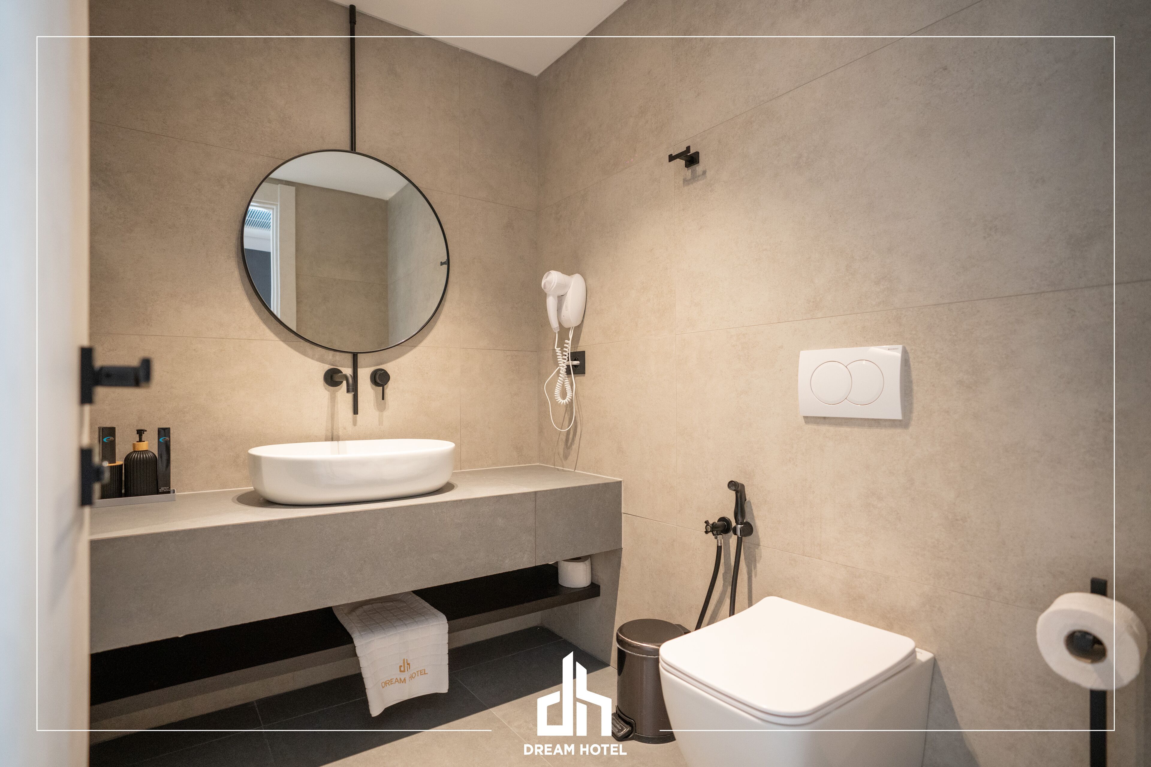 A modern bathroom with a round mirror, a sink, a toilet, and a hairdryer.