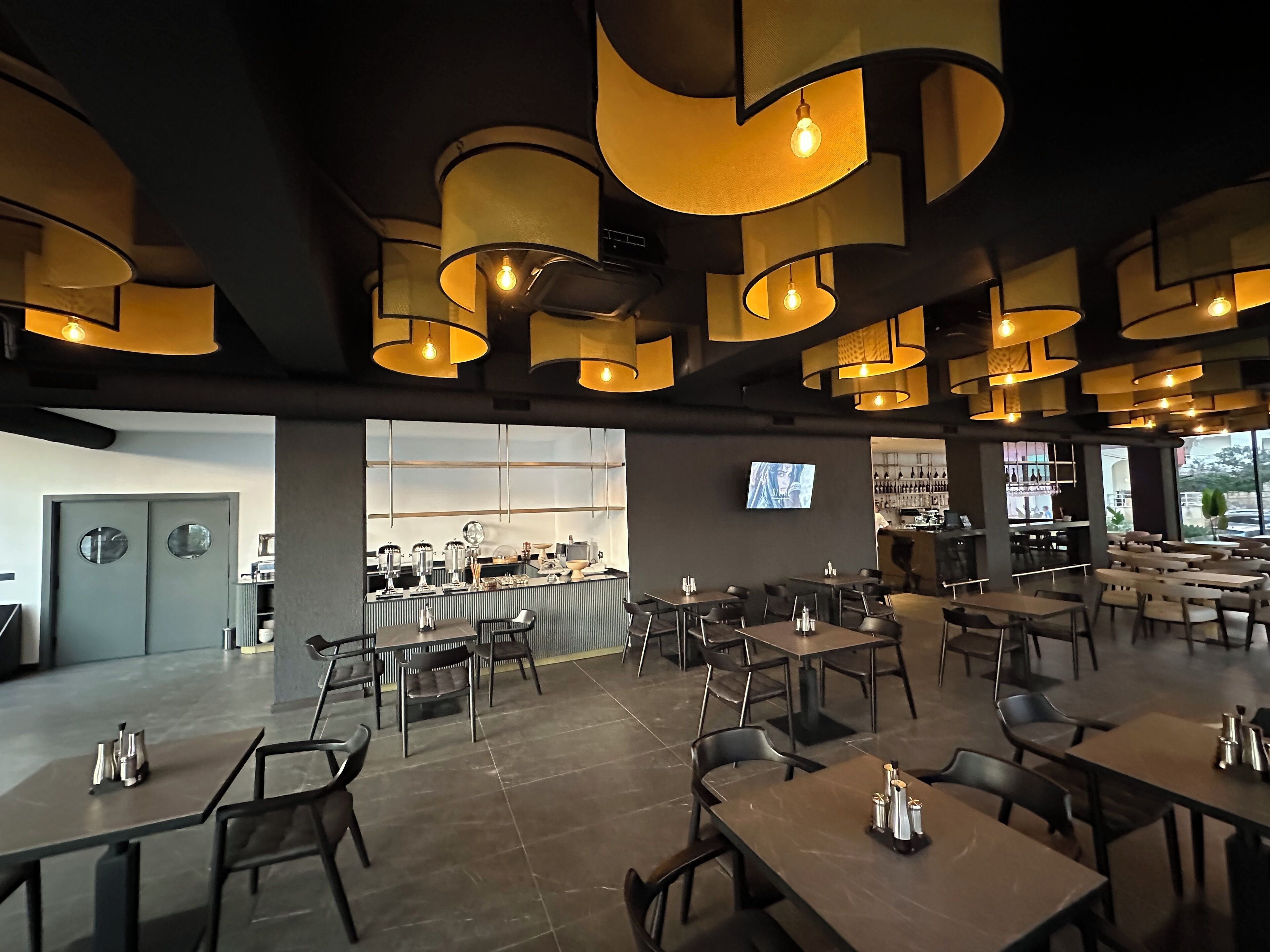 A modern restaurant with a bar area, multiple seating arrangements, and a television screen on the wall.