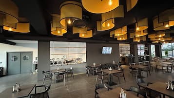 A modern restaurant with a bar area, multiple seating arrangements, and a television screen on the wall.