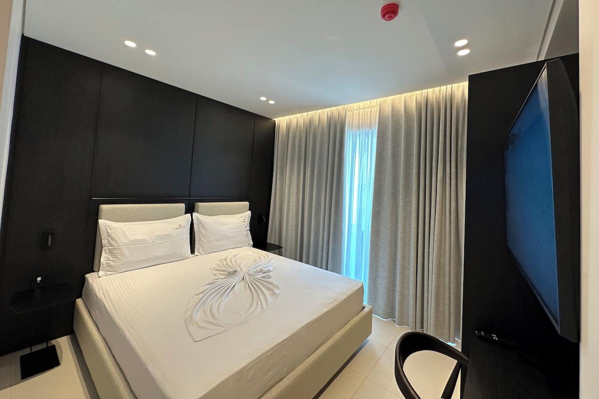 Ein modernes Hotelzimmer mit einem großen Bett, dunklen Wänden und einem Flachbildfernseher.