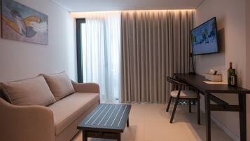 Una sala de estar moderna con un sofá, una mesa de centro, una mesa de comedor con sillas, un televisor montado en la pared y un ventanal con cortinas.