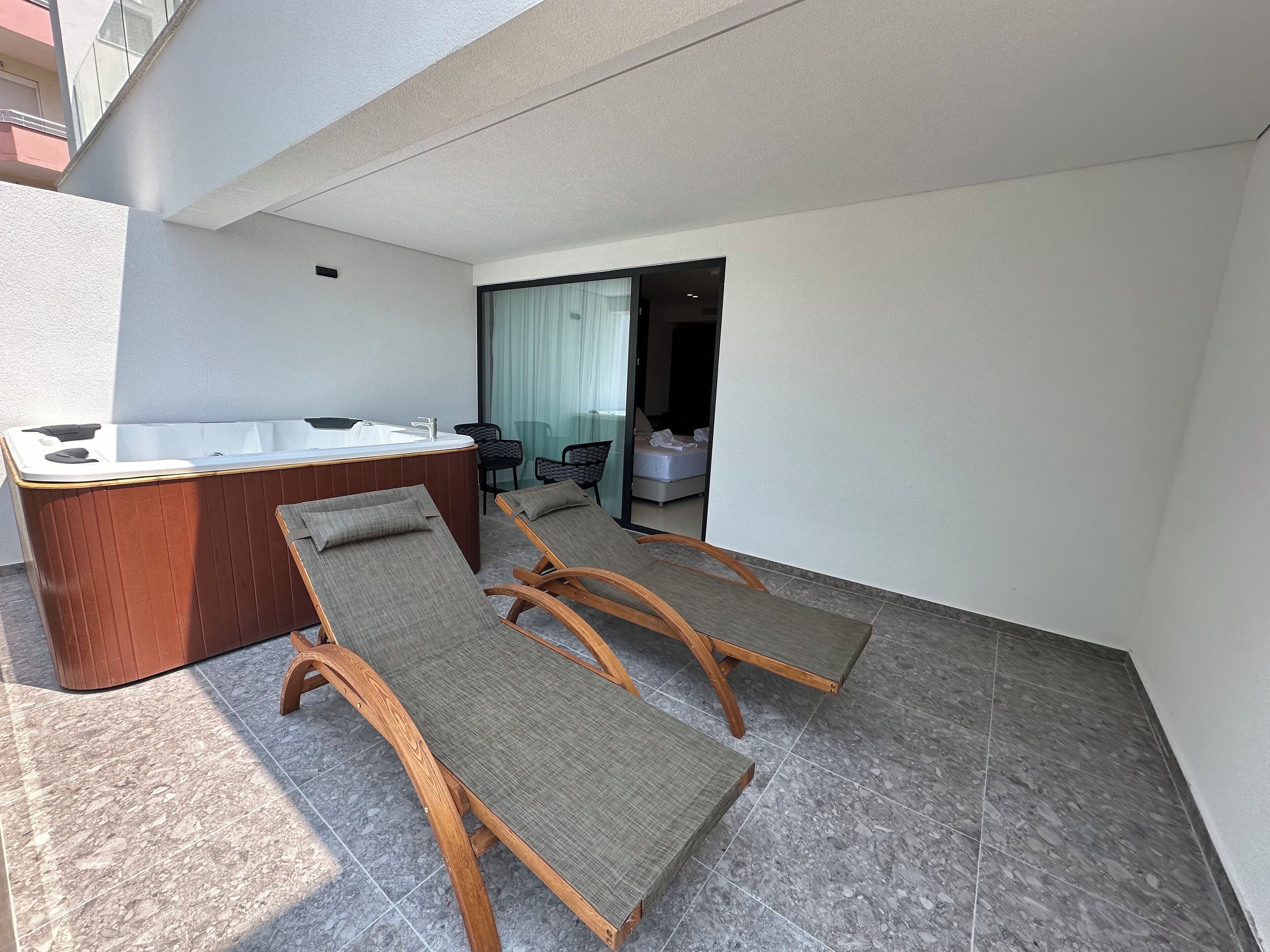 A balcony with a hot tub, two lounge chairs, and a bed in the background.