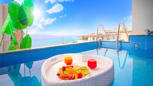 A poolside setting with a wicker chair, fruits, and drinks. - DREAM HOTEL SARANDA (Sarandë)