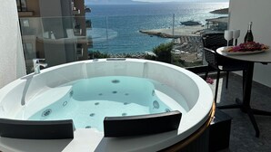 A balcony with a hot tub, a table with two glasses and a bottle, and a view of the sea and distant mountains. - DREAM HOTEL SARANDA (Sarandë)