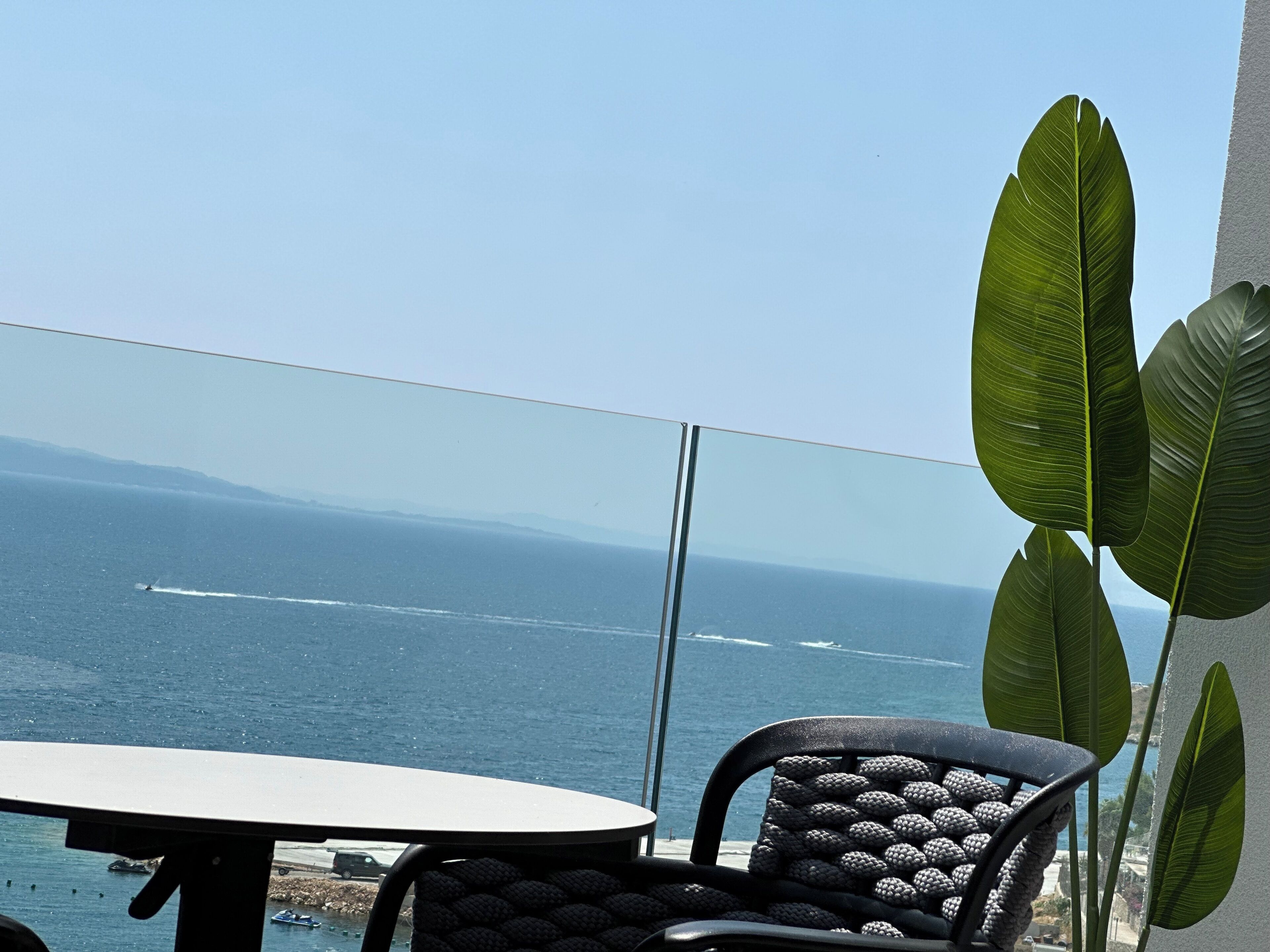 A balcony with a view of the ocean, a table, and a chair.