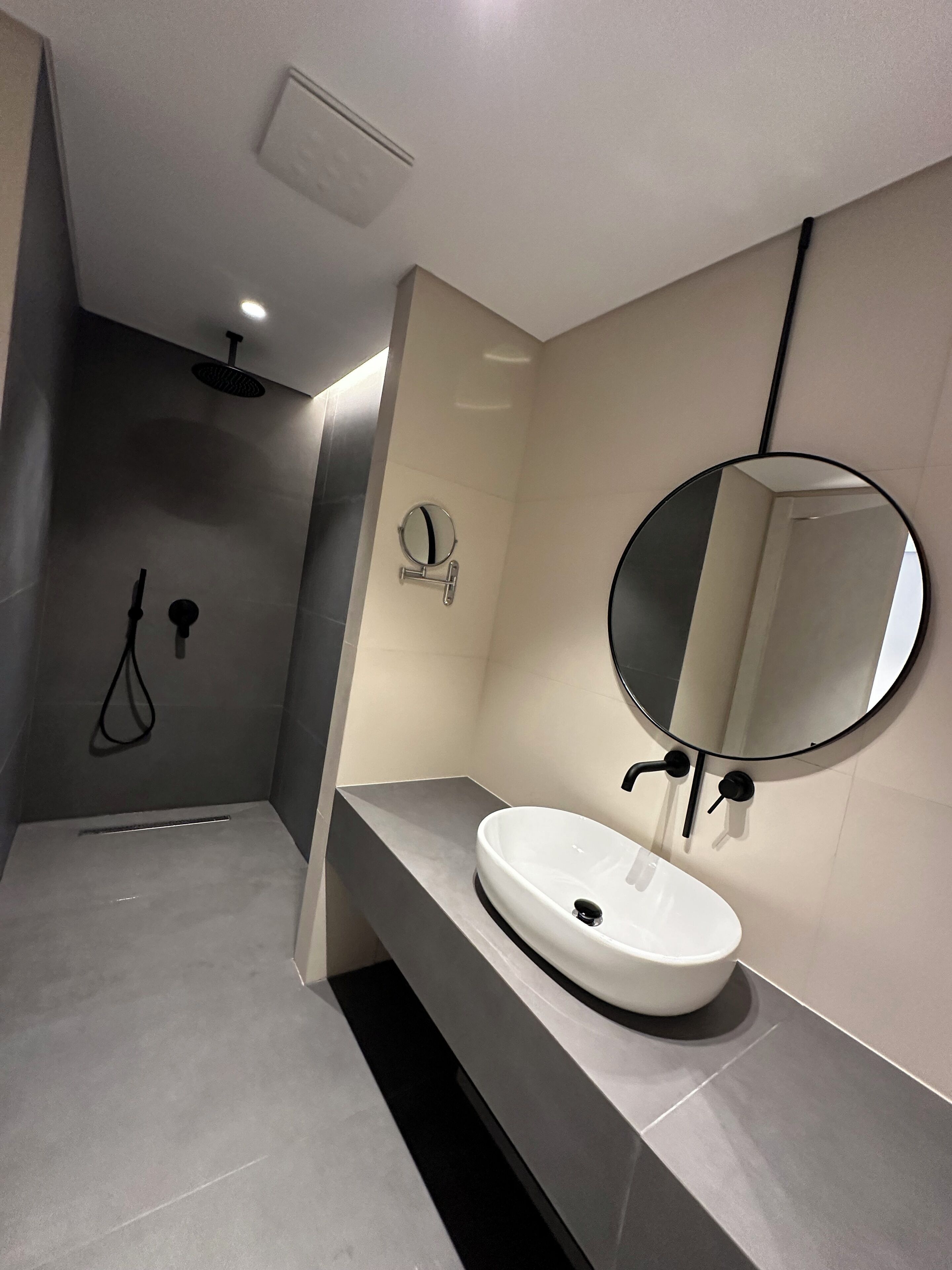 A modern bathroom with a round mirror, a white sink, and a shower area.
