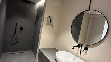 A modern bathroom with a round mirror, a white sink, and a shower area.