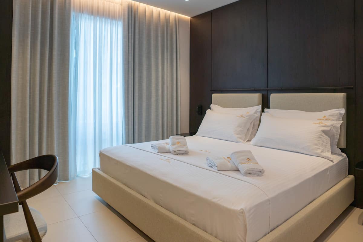 Ein Hotelzimmer mit einem großen Bett, zwei Kissen, einer ordentlich bezogenen Tagesdecke, einem Stuhl und einem Schreibtisch.