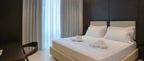 Una habitación de hotel con una cama grande, dos almohadas, una colcha impecable, una silla y un escritorio.