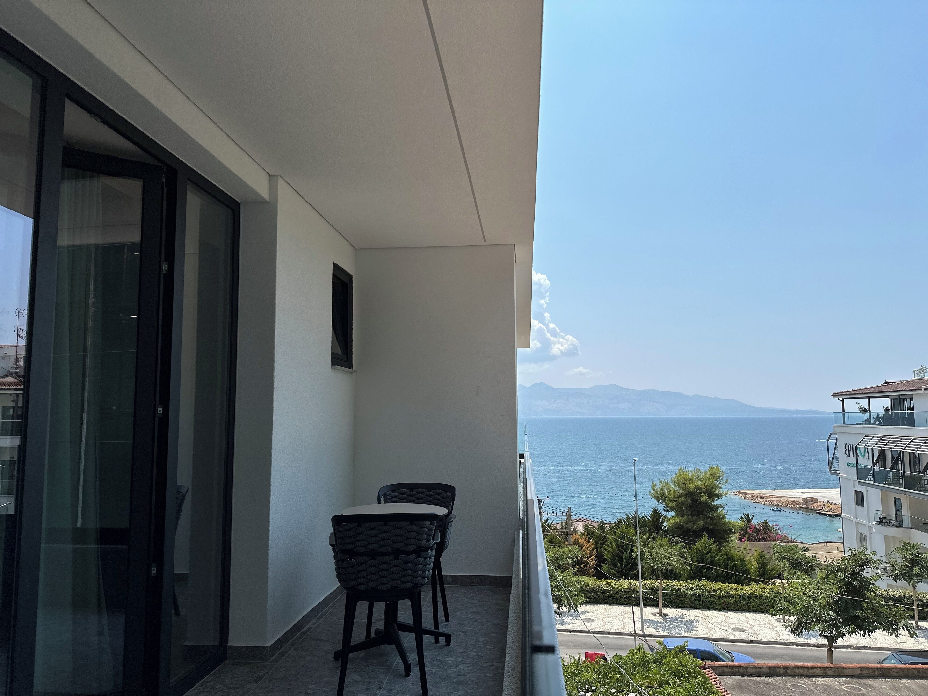 A balcony with two chairs, a view of the sea, and a building with a balcony.