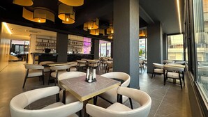 A modern restaurant interior with round tables, cushioned chairs, pendant lighting, and a bar area with shelves of bottles. - DREAM HOTEL SARANDA (Sarandë)