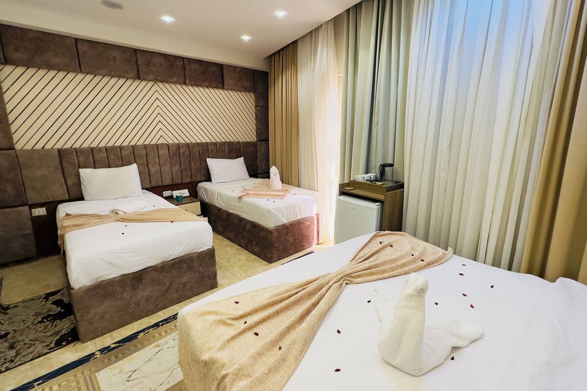 A hotel room with two beds, a minibar, and a large window with curtains.