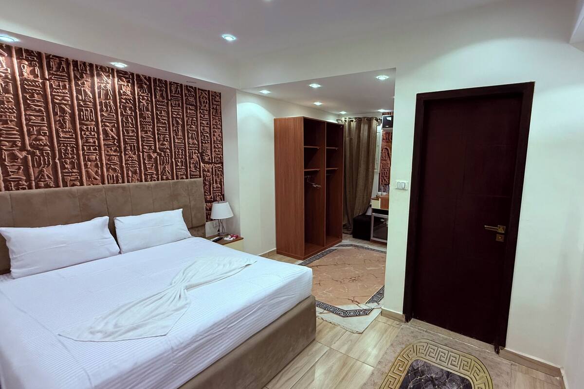 A hotel room with a large bed, a wardrobe, a TV, and a patterned wall.