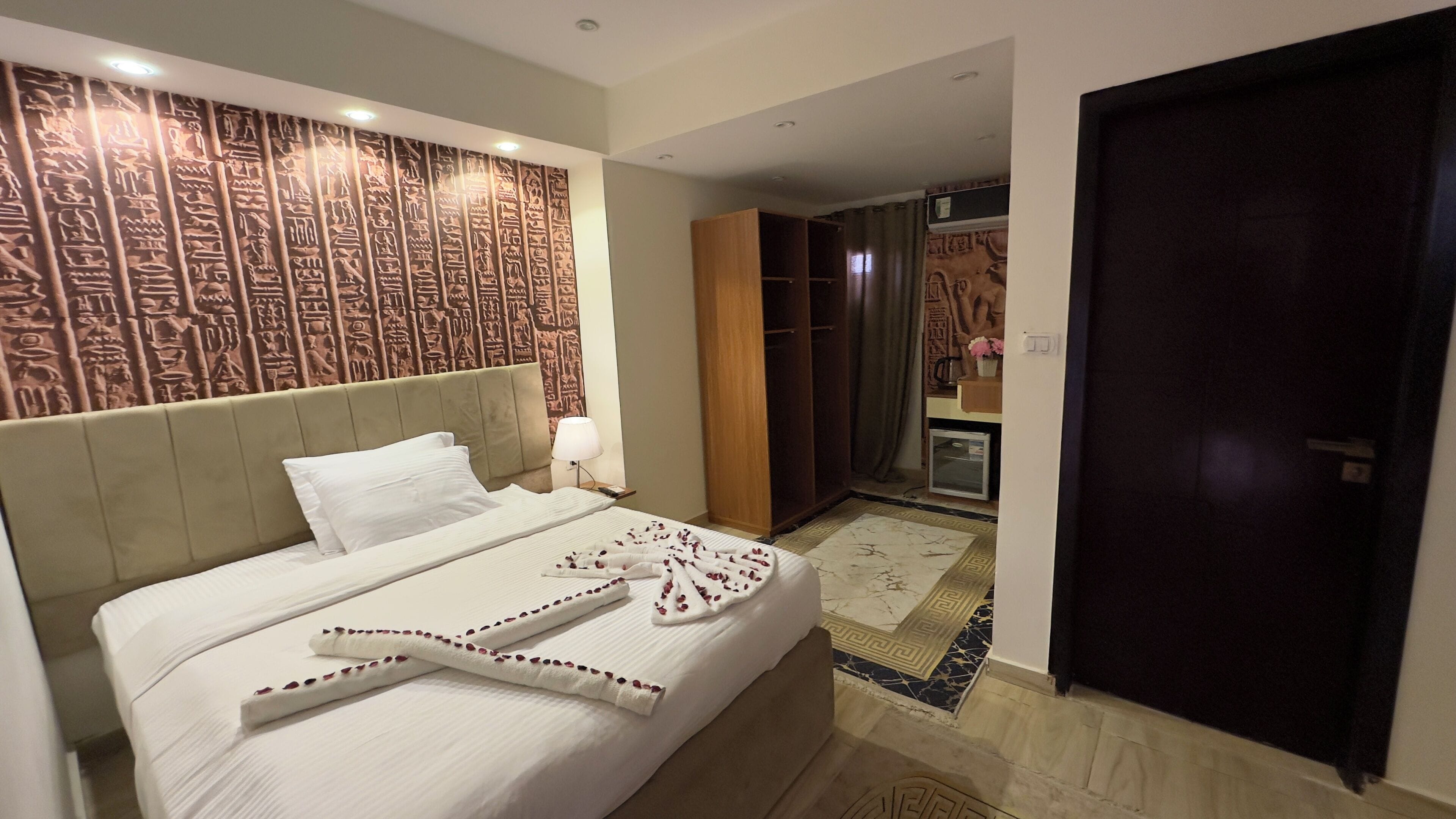 Habitación de hotel con cama, mesita de noche, armario y baño visible a través de una puerta abierta.