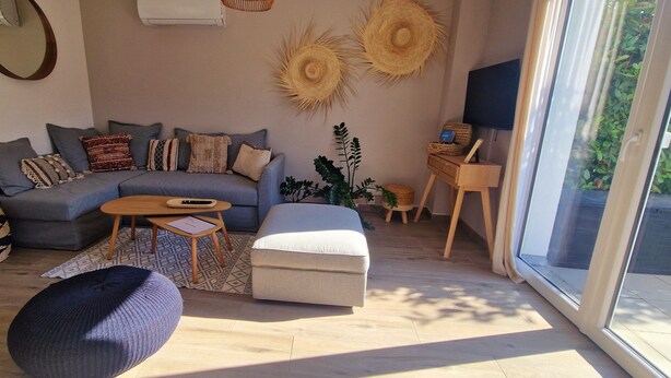 Una sala de estar moderna con un sofá seccional gris, una mesita redonda pequeña, un sillón azul y un ventanal con vistas a zonas verdes.