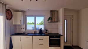 Una cocina compacta con armarios blancos, encimera negra, horno empotrado y ventana con vistas a zonas verdes.