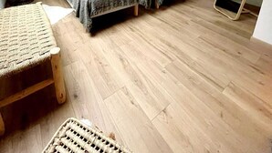 Un dormitorio con dos camas, piso de madera, una mesita y un espejo.
