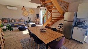 Una cocina moderna con refrigerador, microondas y horno integrados. Hay una mesa de comedor de madera con sillas y un amplio ventanal que proporciona luz natural.