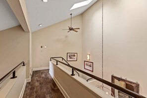 A staircase with a wooden handrail, a ceiling fan, and framed pictures on the wall.
