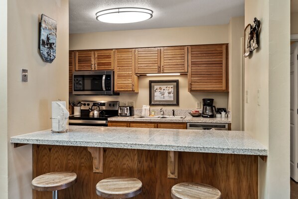 A kitchen with wooden cabinets, a granite countertop, a microwave, a coffee maker, and a sink.