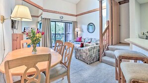 A cozy living area with a wooden dining table, chairs, a patterned sofa, and a staircase leading to an upper level.
