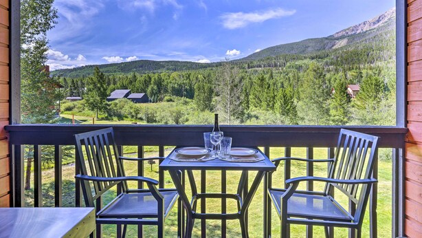 A balcony with a table set for two, overlooking a mountainous landscape.