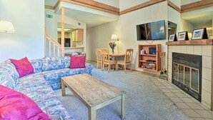 A living room with a sectional sofa, a coffee table, a fireplace, a television, and a dining area with a table and chairs.