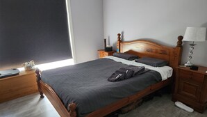 A neatly made bed with a wooden headboard, a bedside table with a lamp, and a small nightstand with a clock. - Short term stay perfect for the business traveller
Pet friendly
 (Griffith)