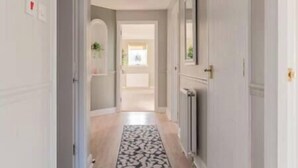 A hallway with a patterned rug, a radiator, and a door leading to another room. - Penthouse at the Bay near Edinburgh (Dalgety Bay)