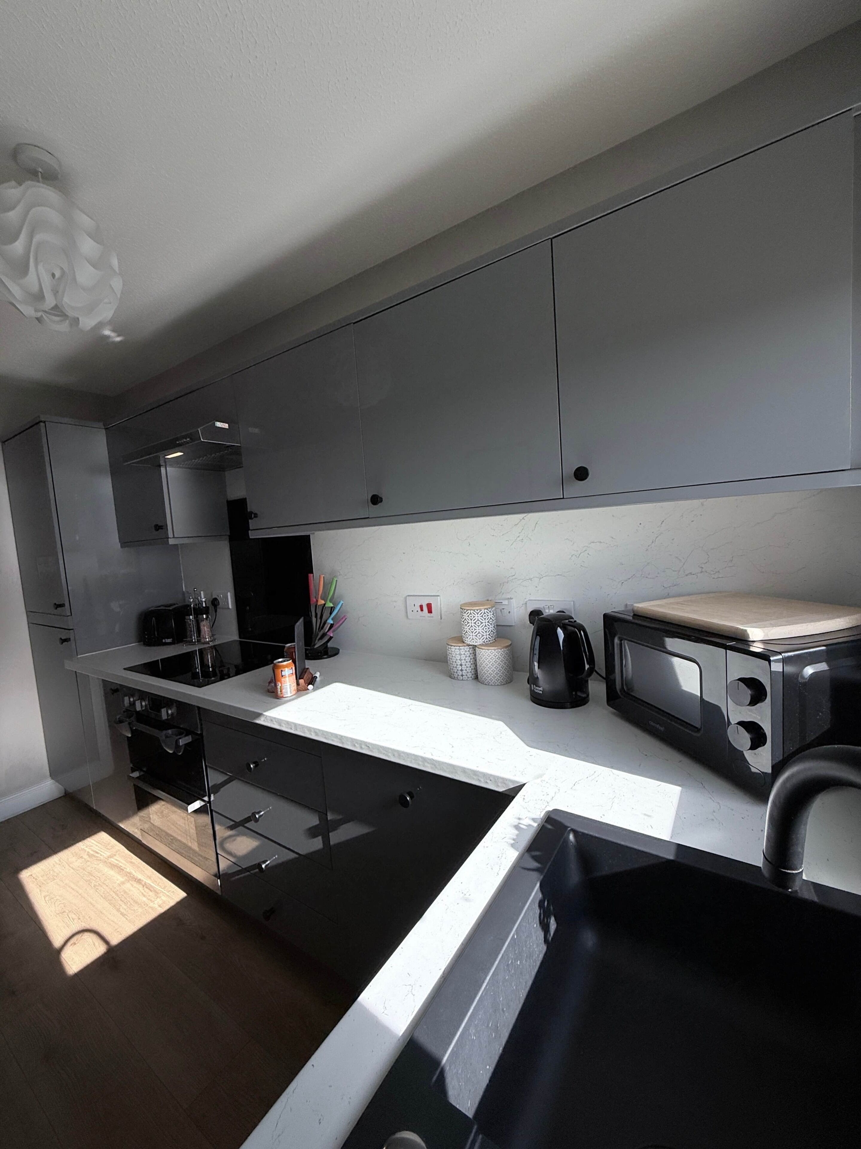 Une cuisine moderne avec des meubles gris, un micro-ondes noir et un évier.