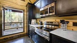 A modern kitchen with dark cabinetry, stainless steel appliances, and a view of the outdoors through a large window.