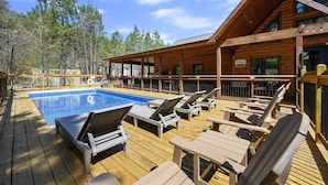 A wooden deck with a swimming pool, lounge chairs, and a covered area with a sign indicating a restaurant.