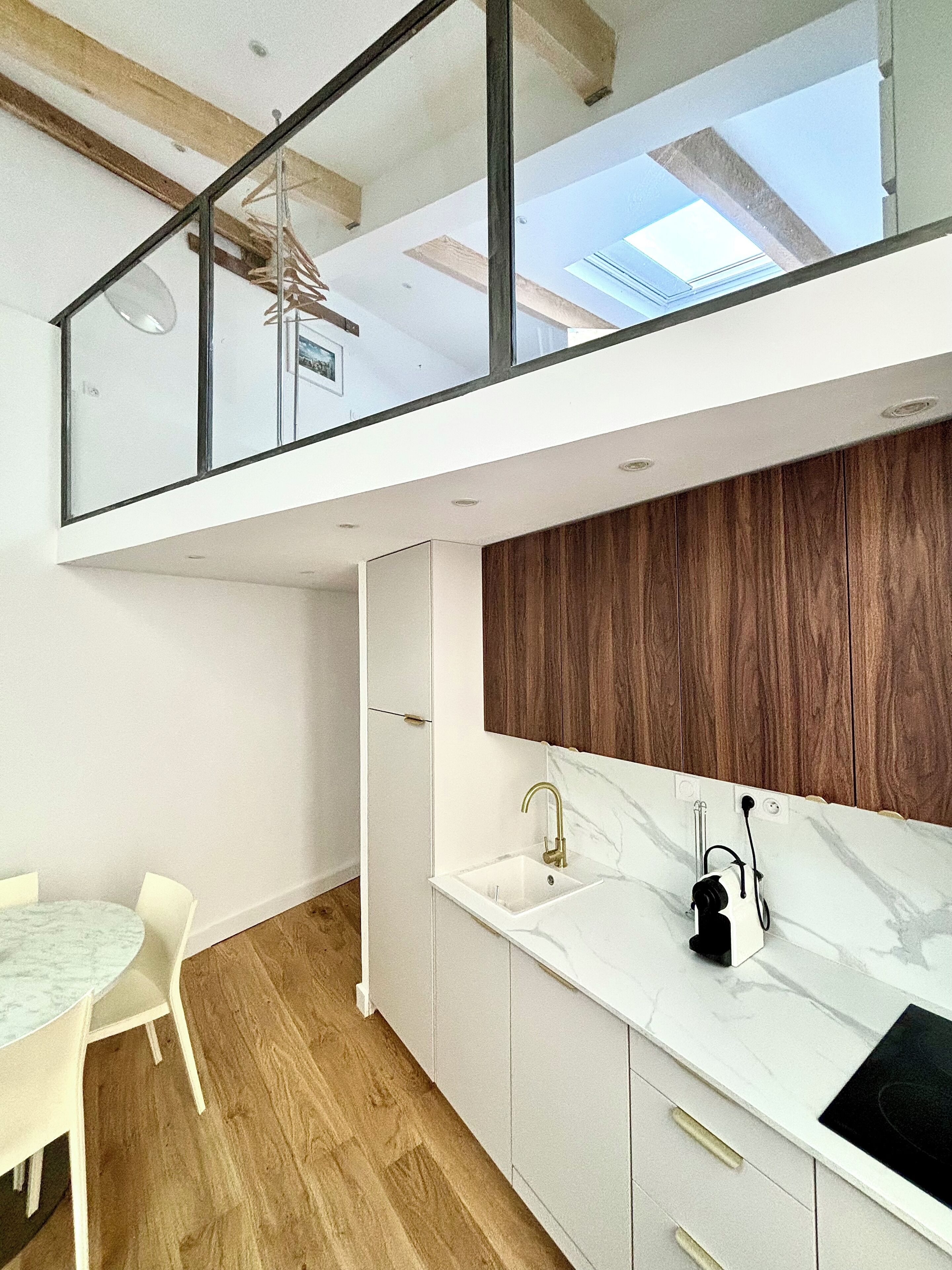 A modern kitchen with a marble countertop, wooden panel backsplash, and a glass railing overlooking a dining area.