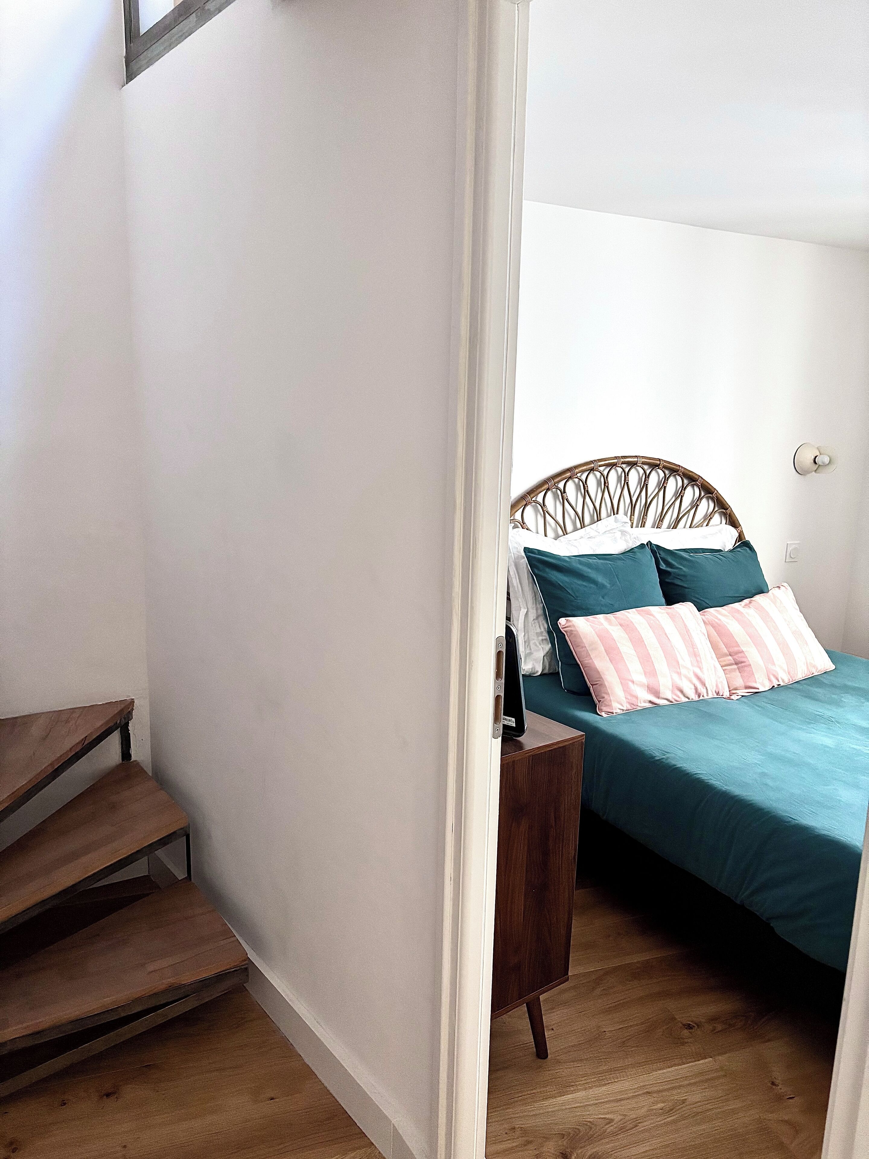 A bedroom with a bed, a nightstand, and a wooden staircase.