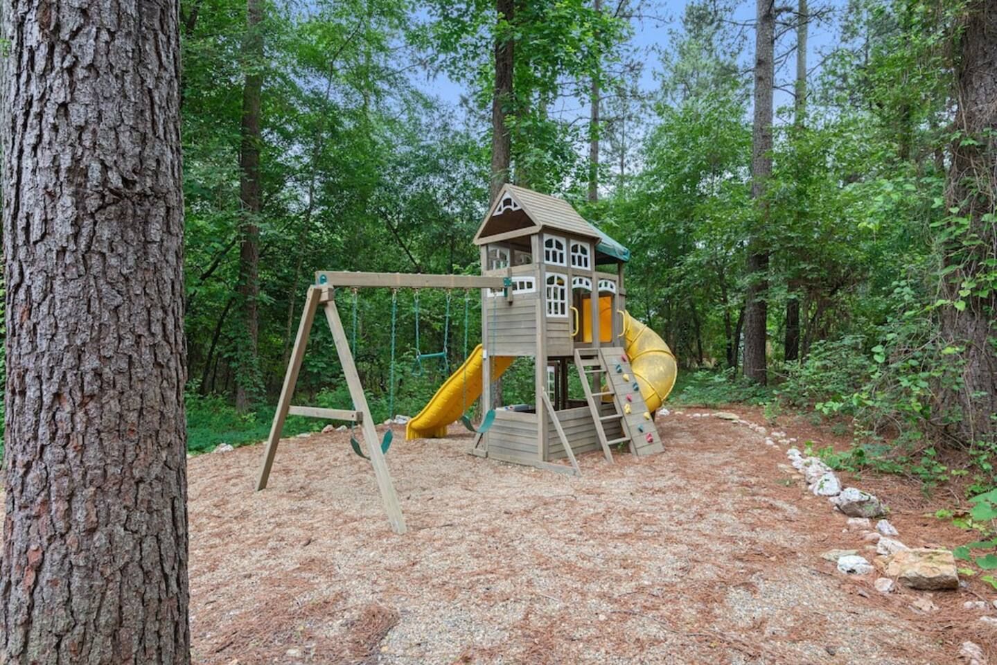 Eine hölzerne Spielanlage mit Rutsche und Kletterstufen in einem bewaldeten Gebiet.
