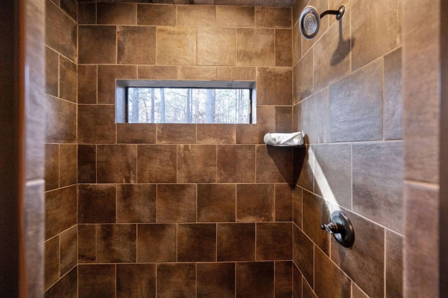Une douche aux carreaux bruns, une fenêtre et un porte-serviettes.