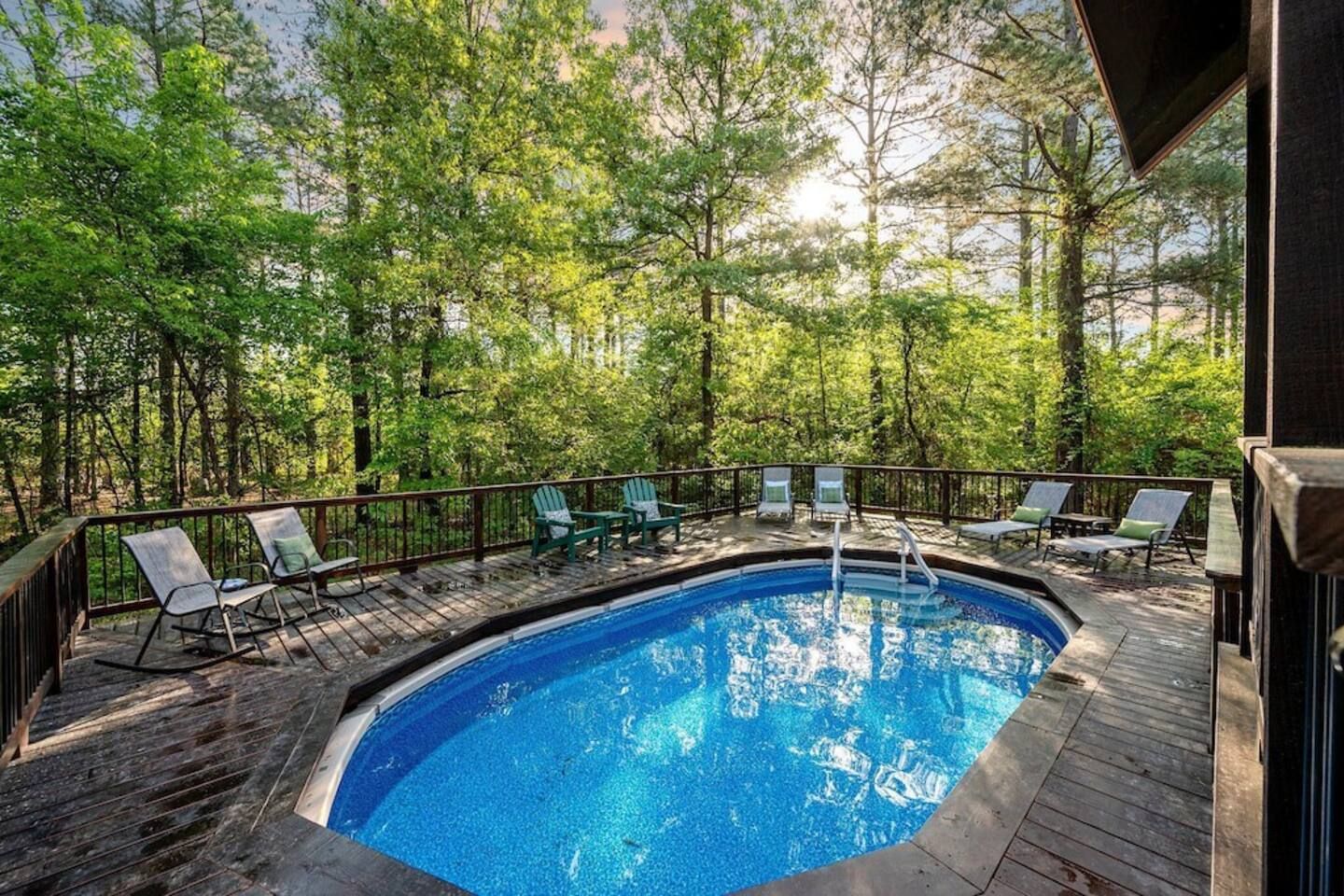 A swimming pool with deck chairs, surrounded by trees.