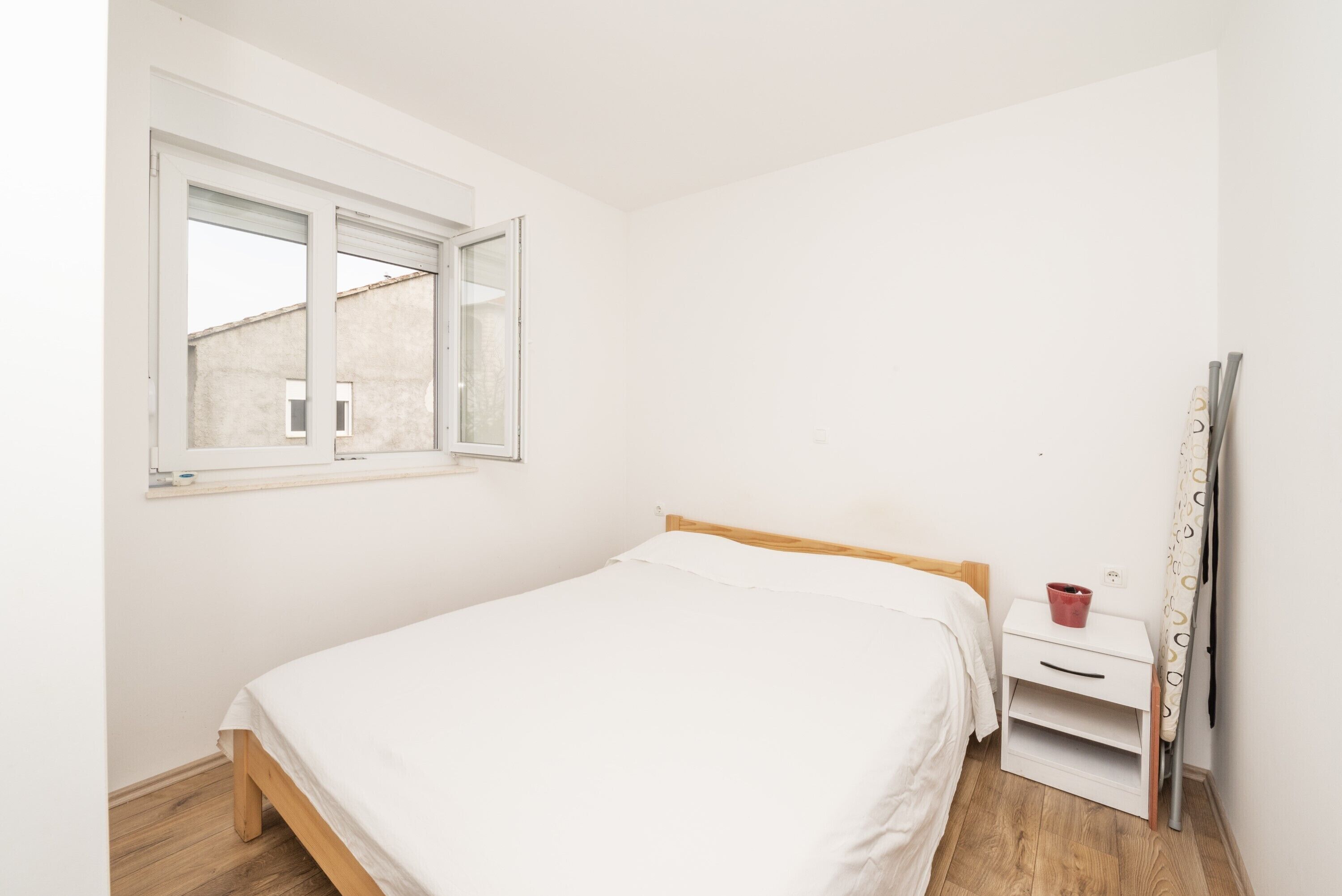 A single bed with a wooden headboard in a room with white walls and a window.