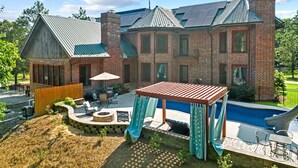 Una casa grande de ladrillo con piscina, mobiliario exterior y un pérgola.