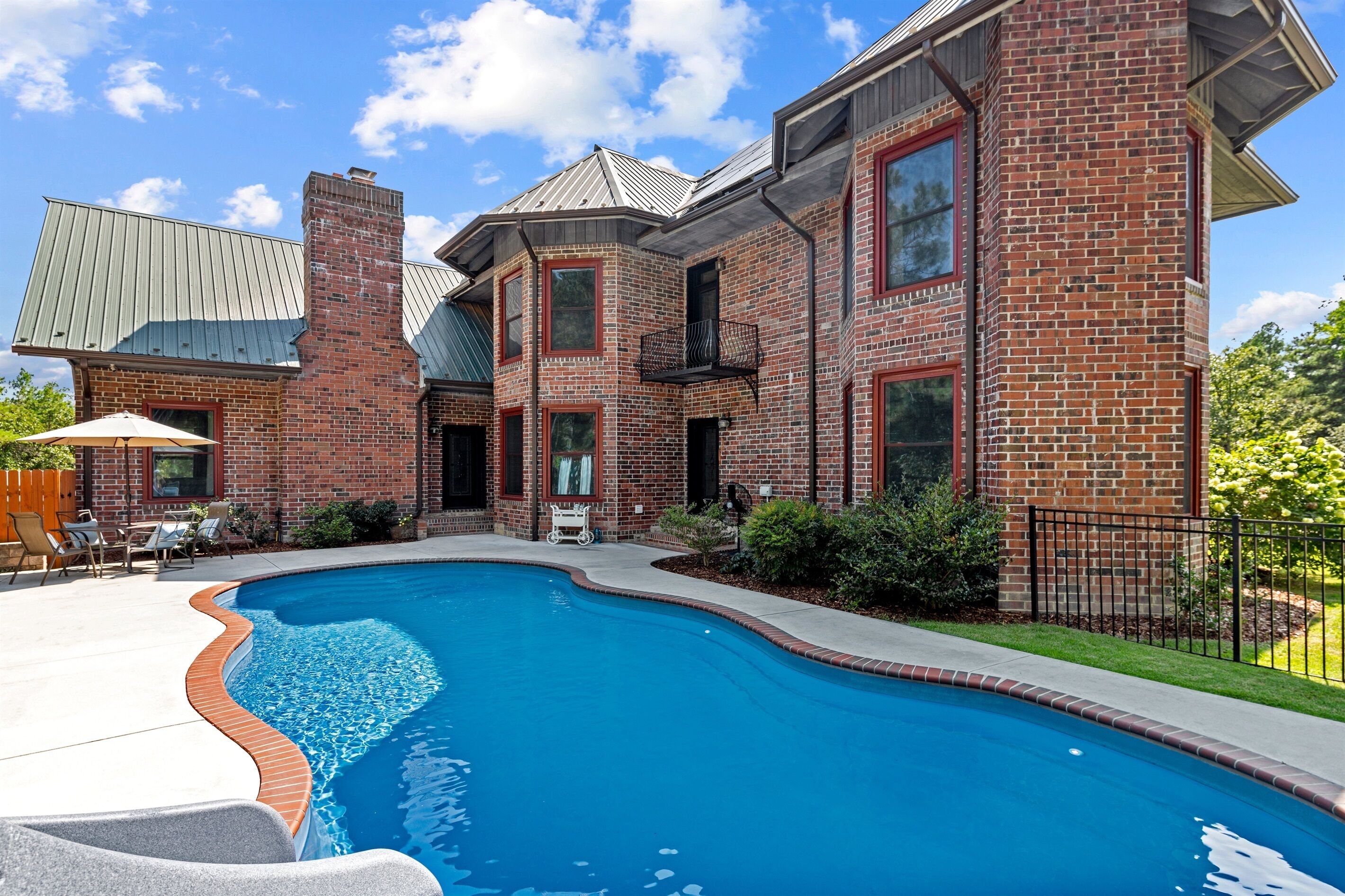 A brick house with a swimming pool, outdoor furniture, and a fenced yard.