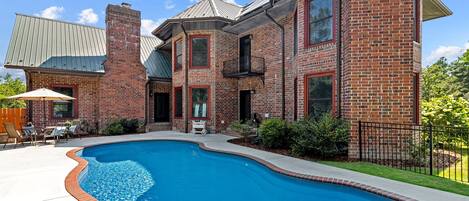 A brick house with a swimming pool, outdoor furniture, and a fenced yard.
