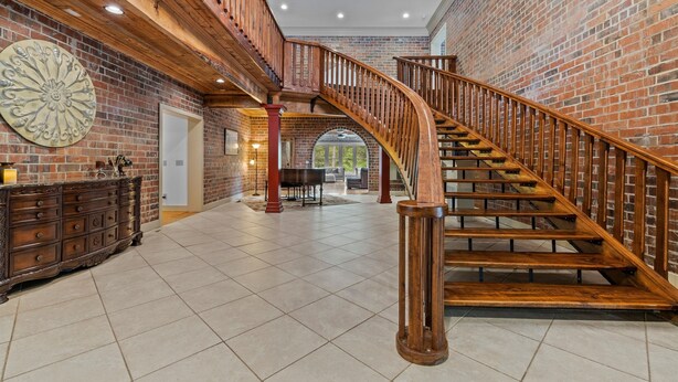 Un interior espacioso con una escalera de madera, paredes de ladrillo y un candelabro.