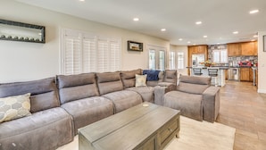 A spacious living area with a large sectional sofa, a coffee table, and a kitchen in the background. - Walk to State Farm Stadium! Poolside Desert Escape (Glendale)